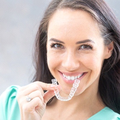 A young woman wearing a green blouse and smiling while preparing to insert Invisalign in Carrollton
