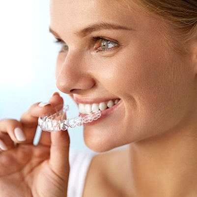 A young female inserting an Invisalign aligner into her mouth