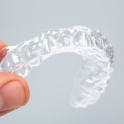 An up-close image of a person holding an Invisalign clear aligner