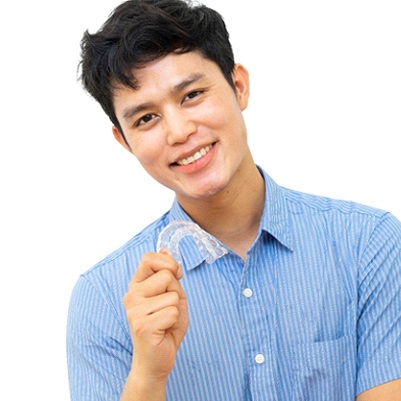 A young male wearing a button-down shirt and holding an Invisalign aligner in his hand