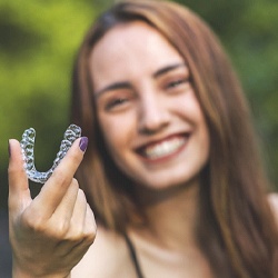 Woman smiling while holding up Invisalign aligner