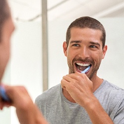 Smiling man in gray shirt brushing teeth in bathroom