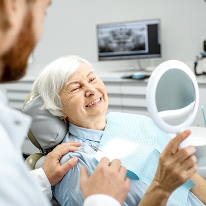 Woman with dentures smiling in dentist's mirror
