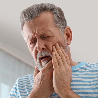 Older man in need of tooth extraction holding jaw