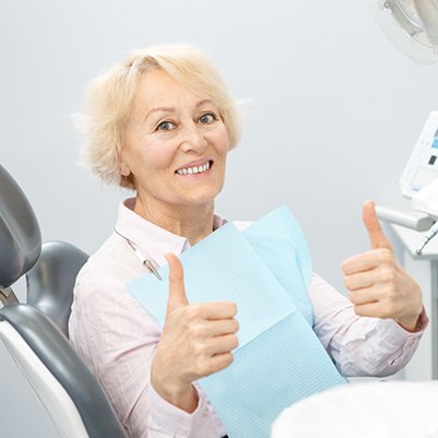 Senior female patient giving thumbs up after receiving implant dentures in Frisco, TX
